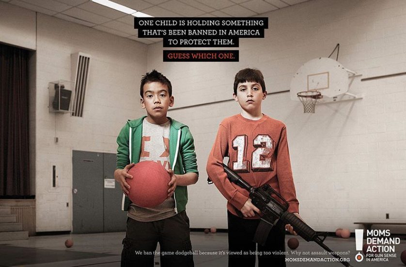 No topo: "Uma criança está segurando algo que é proibido na América para protegê-la. Adivinhe qual." Embaixo: "Nós proibimos o jogo queimada, pois é visto como excessivamente violento. Por que não armas automáticas?" Agência Grey, Toronto, Canadá